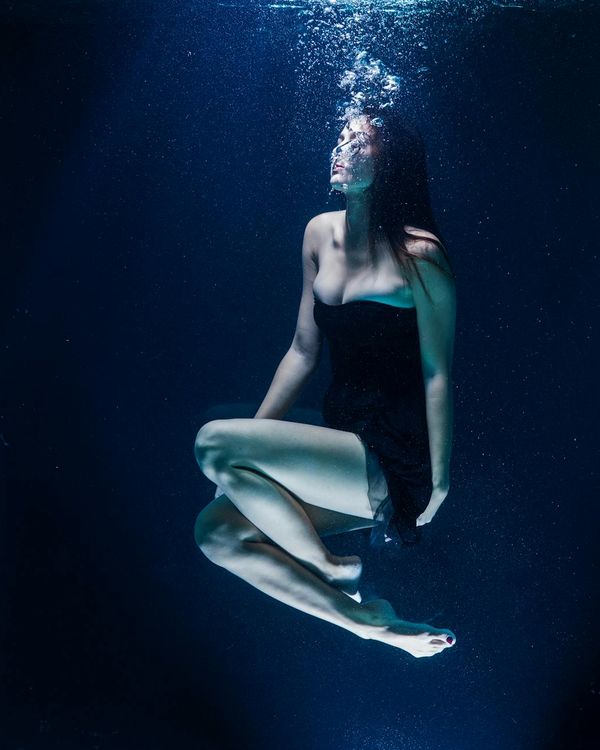 Woman in a calm yoga pose in a dark room with light blue accents.